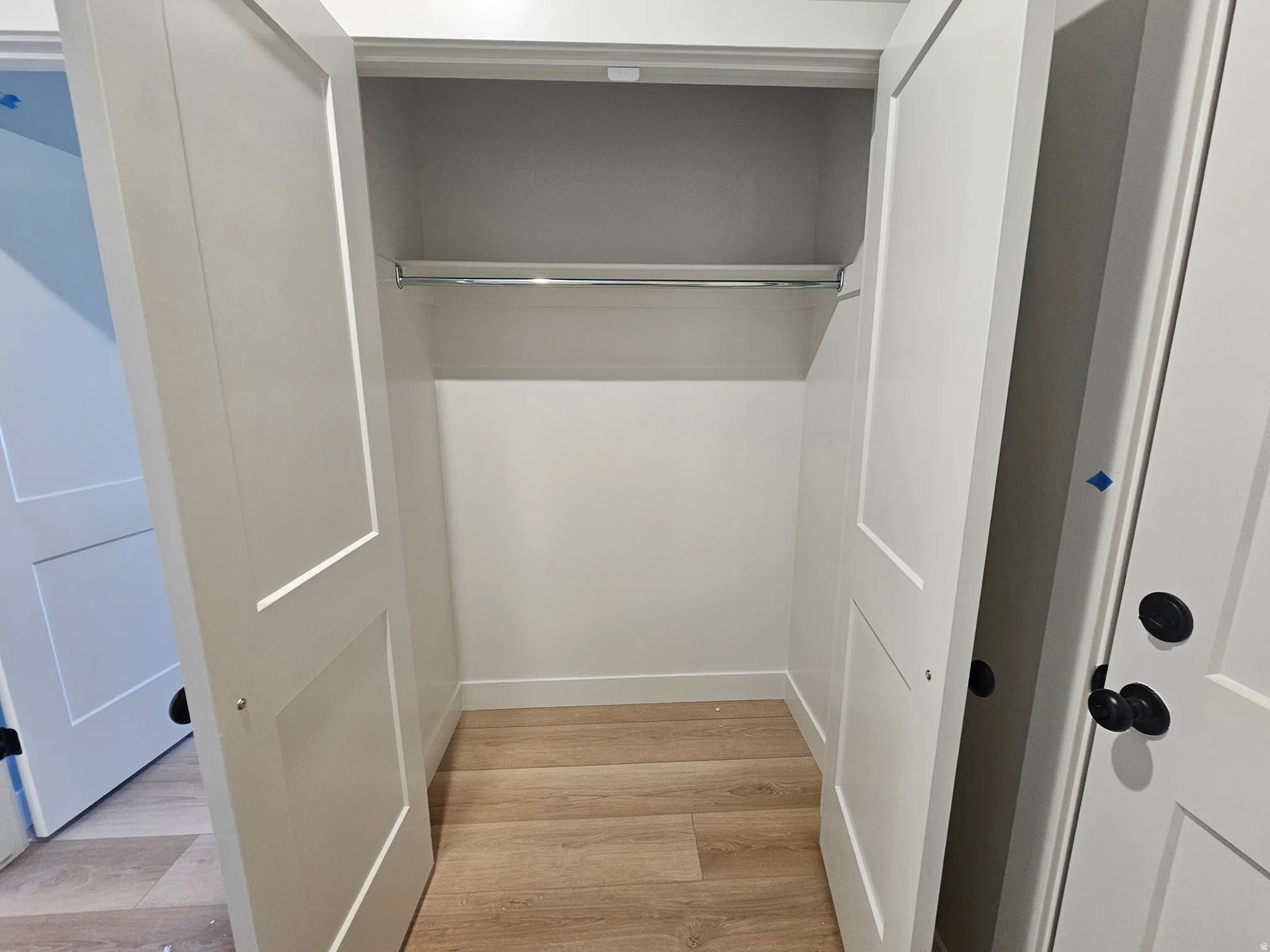 Integrated closet space featuring a built-in hanging rod, light wood-finish flooring, and white baseboards