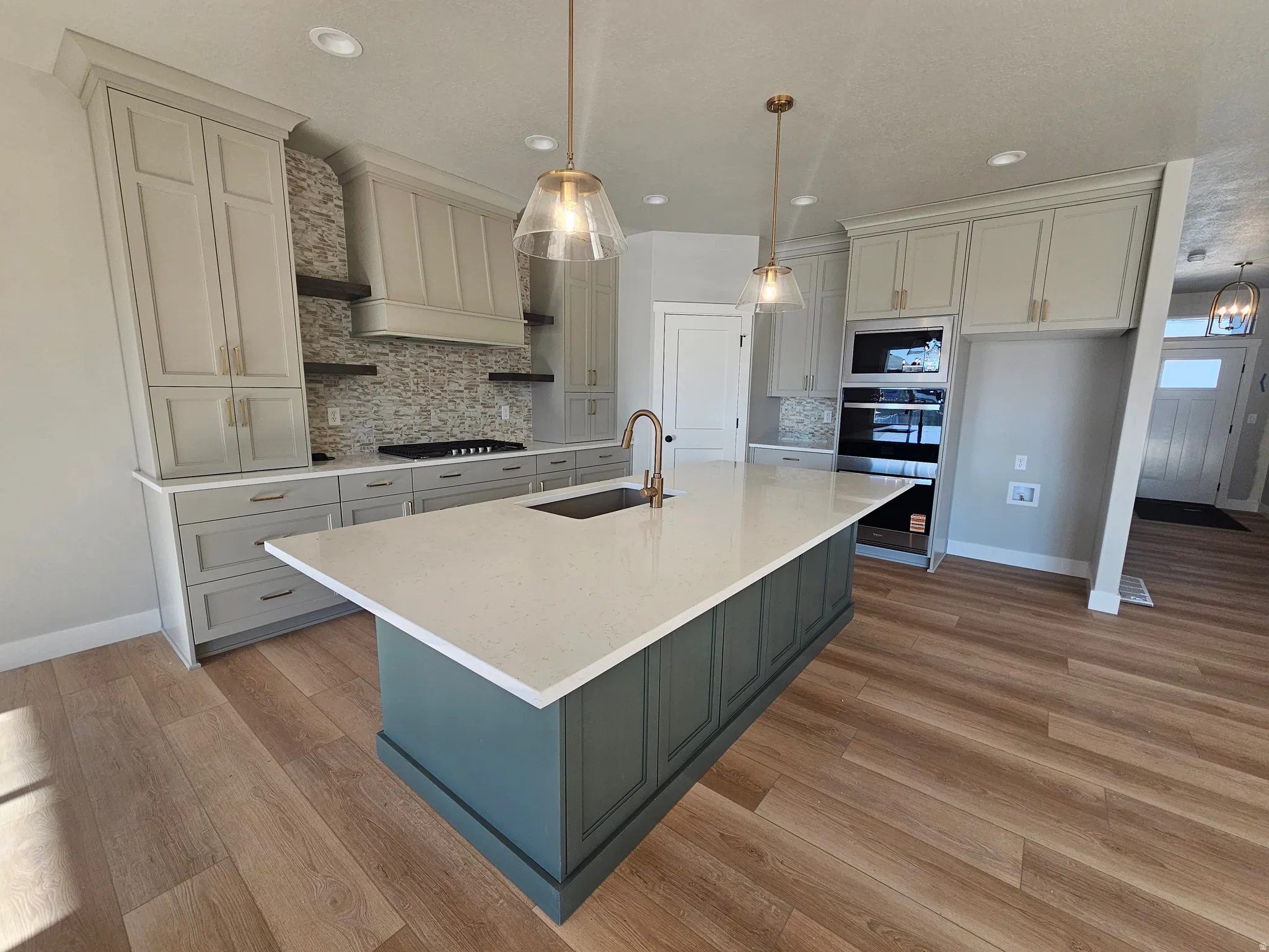 Kitchen featuring a large central island with a light-toned countertop, wood-finish flooring, recessed lighting, built-in stainless steel appliances, and a mosaic tile backsplash