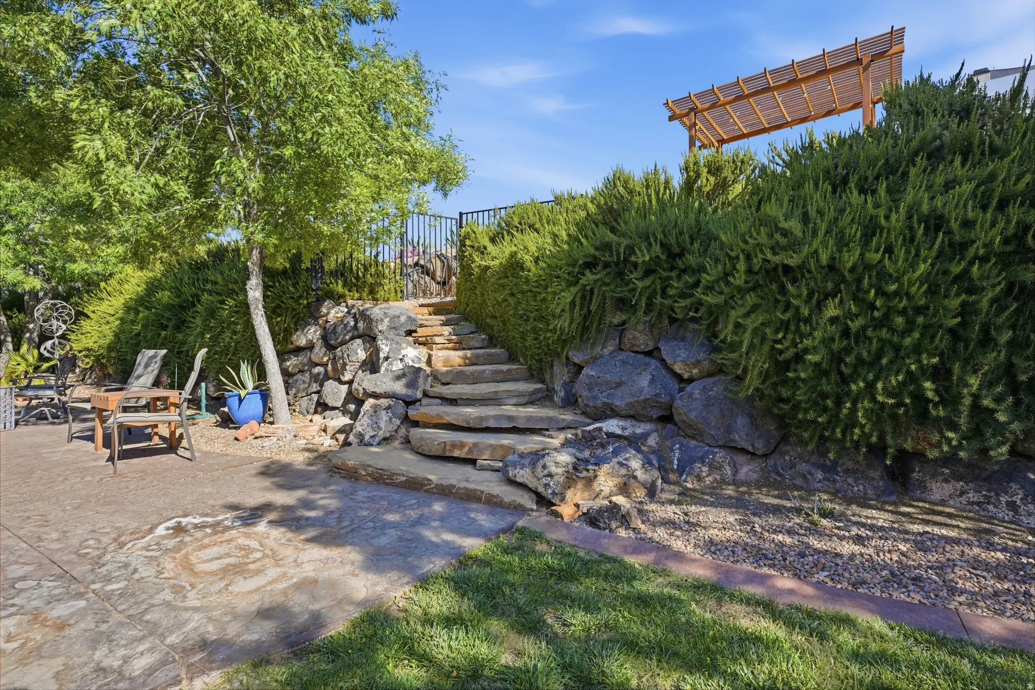 Stone retaining wall with natural stone steps leading to a raised area featuring a wood pergola