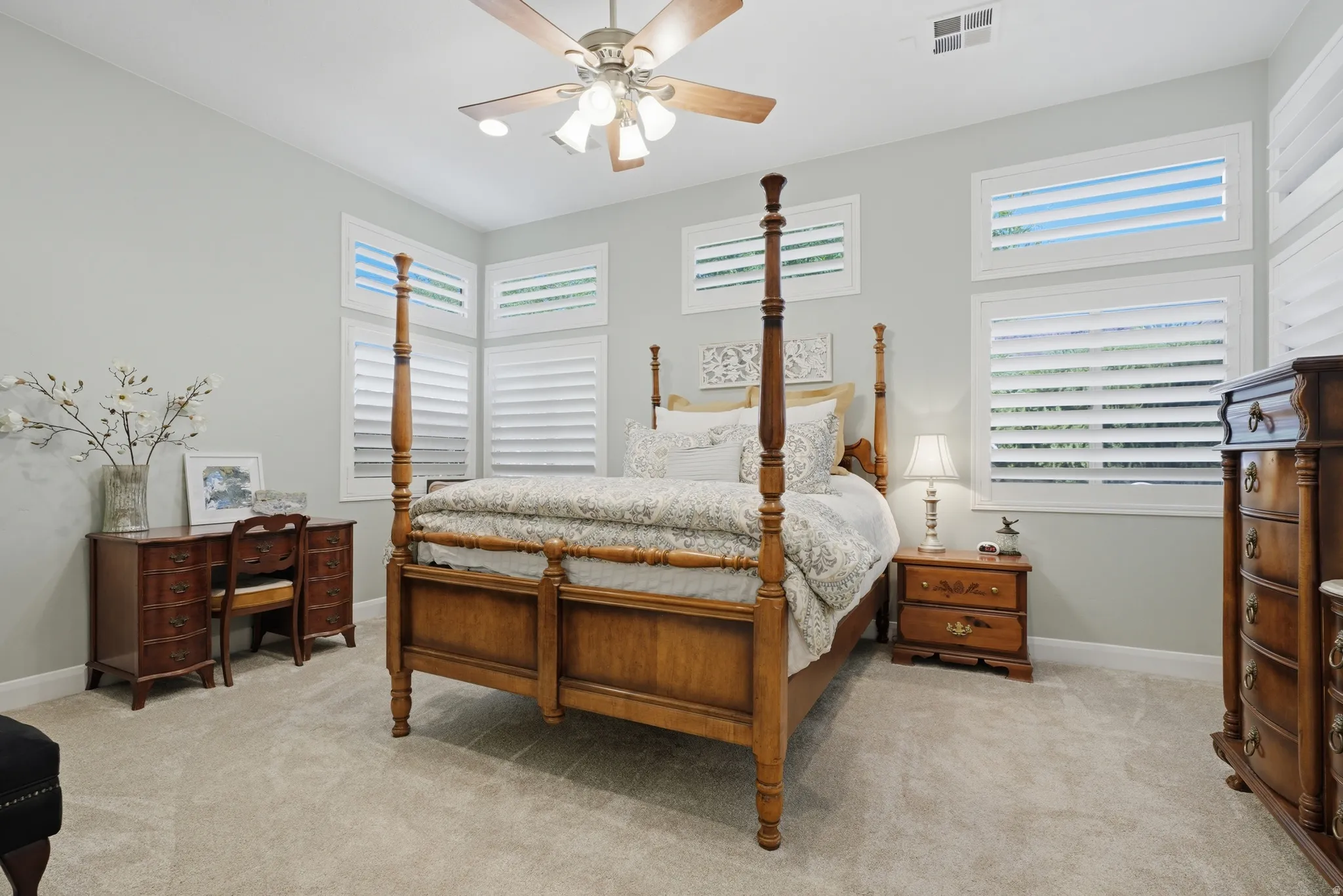 Carpeted room featuring multiple windows with louvered shutters, a ceiling fan with integrated lighting, and light-toned wall paint