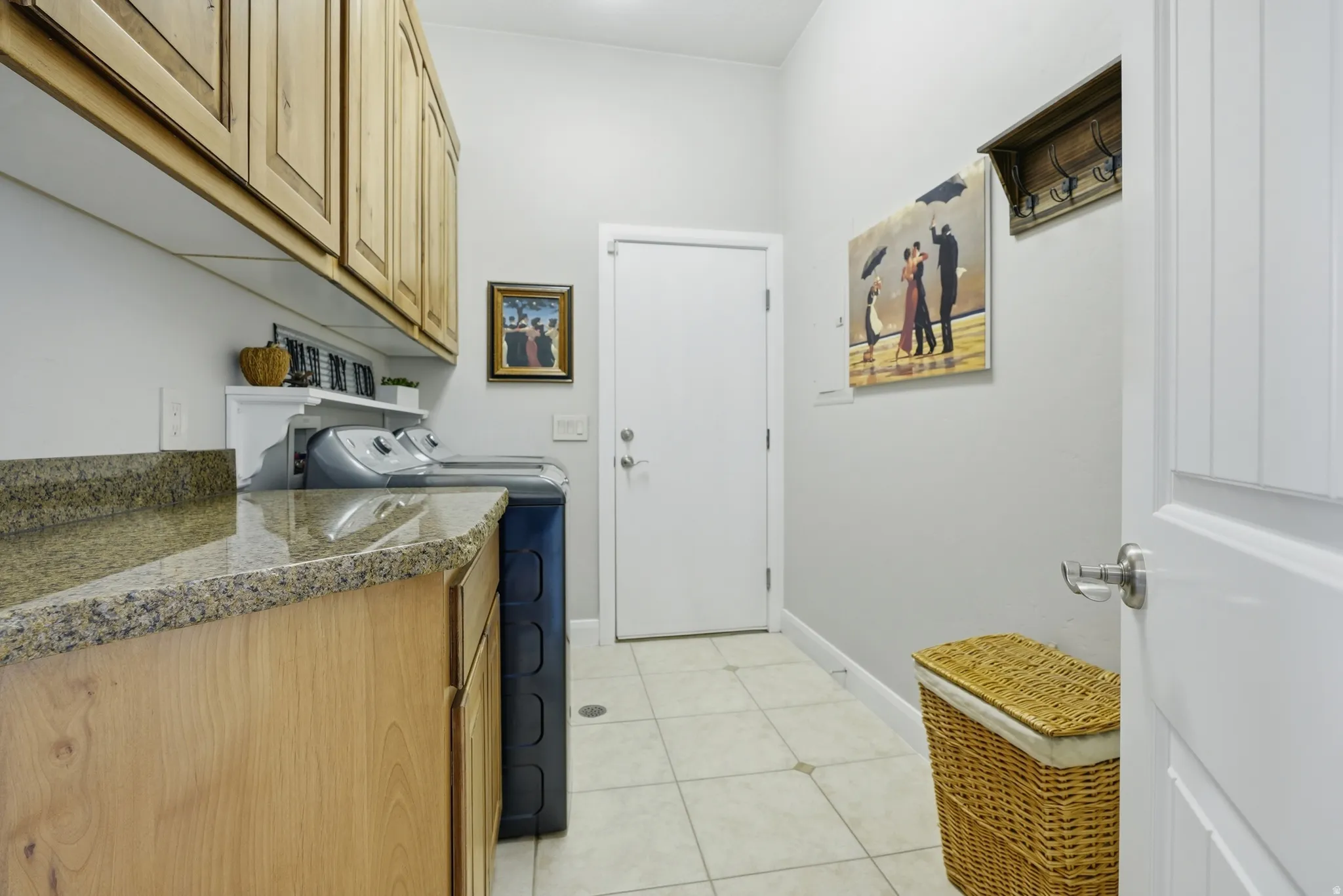 Functional laundry area featuring light wood cabinetry, stone-finish countertops, and tiled flooring