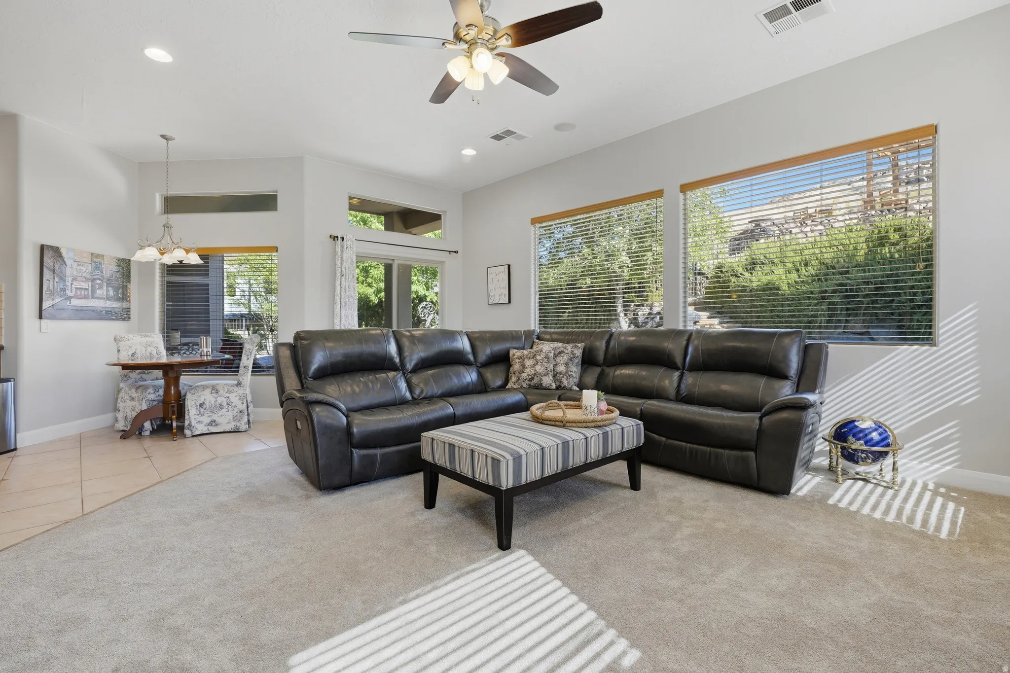 Spacious living area featuring light gray wall paint, an overhead ceiling fan with lighting, recessed lighting, and large windows with horizontal blinds