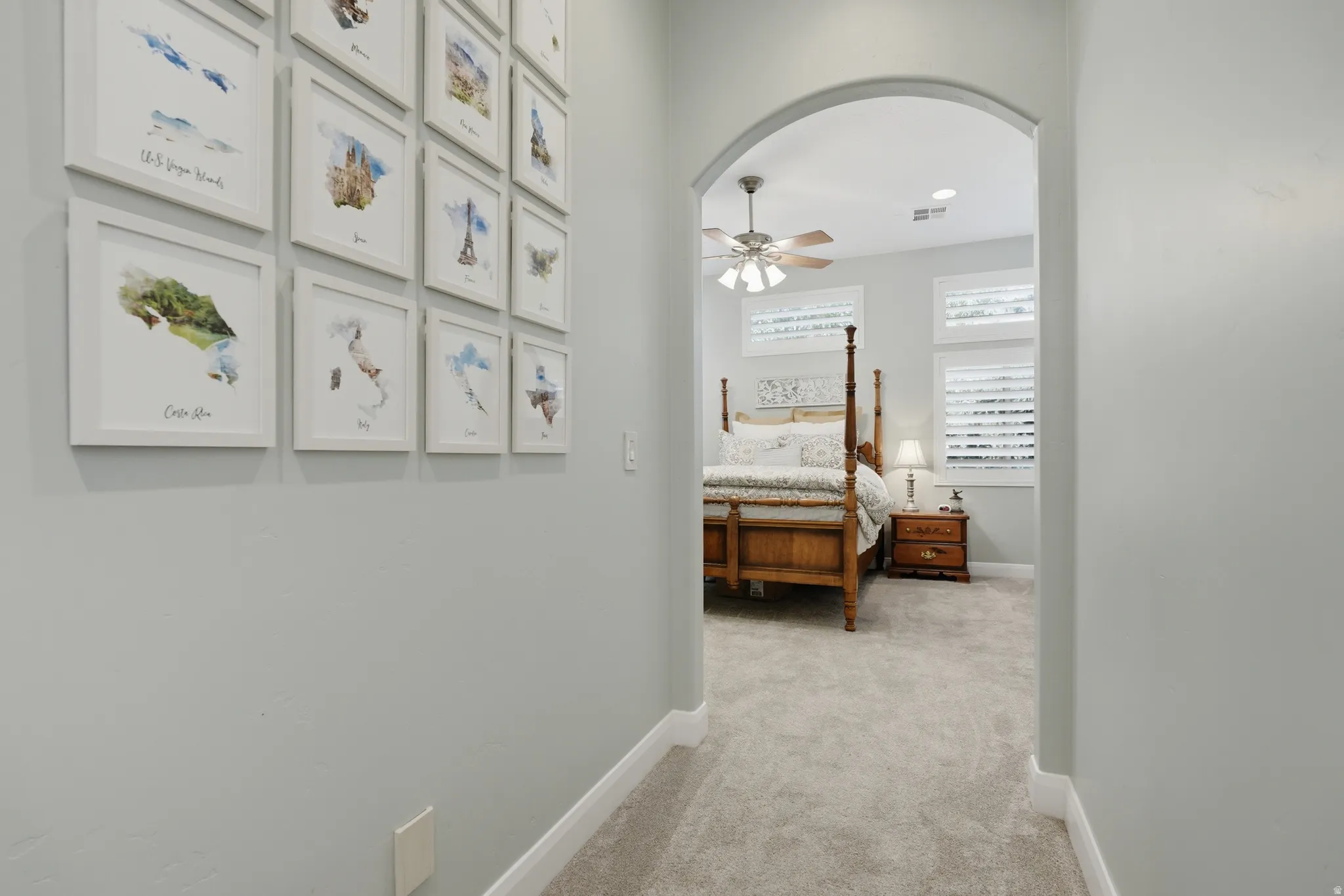 Arched doorway leading to a room featuring light gray walls, plush carpeting, a ceiling fan, and horizontal window blinds