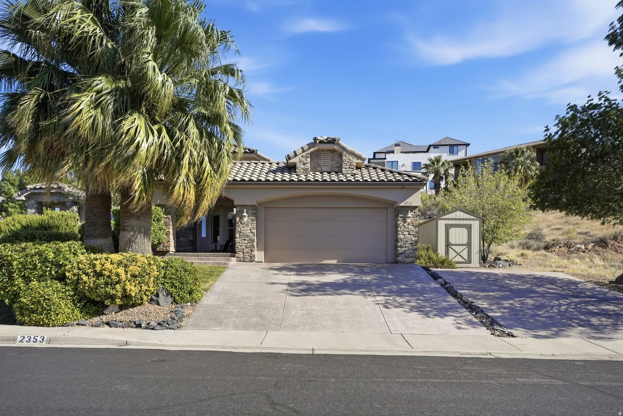 Mediterranean-style residence featuring a stone facade, a tiled roof, an integrated two-car garage, a concrete driveway, and established front landscaping