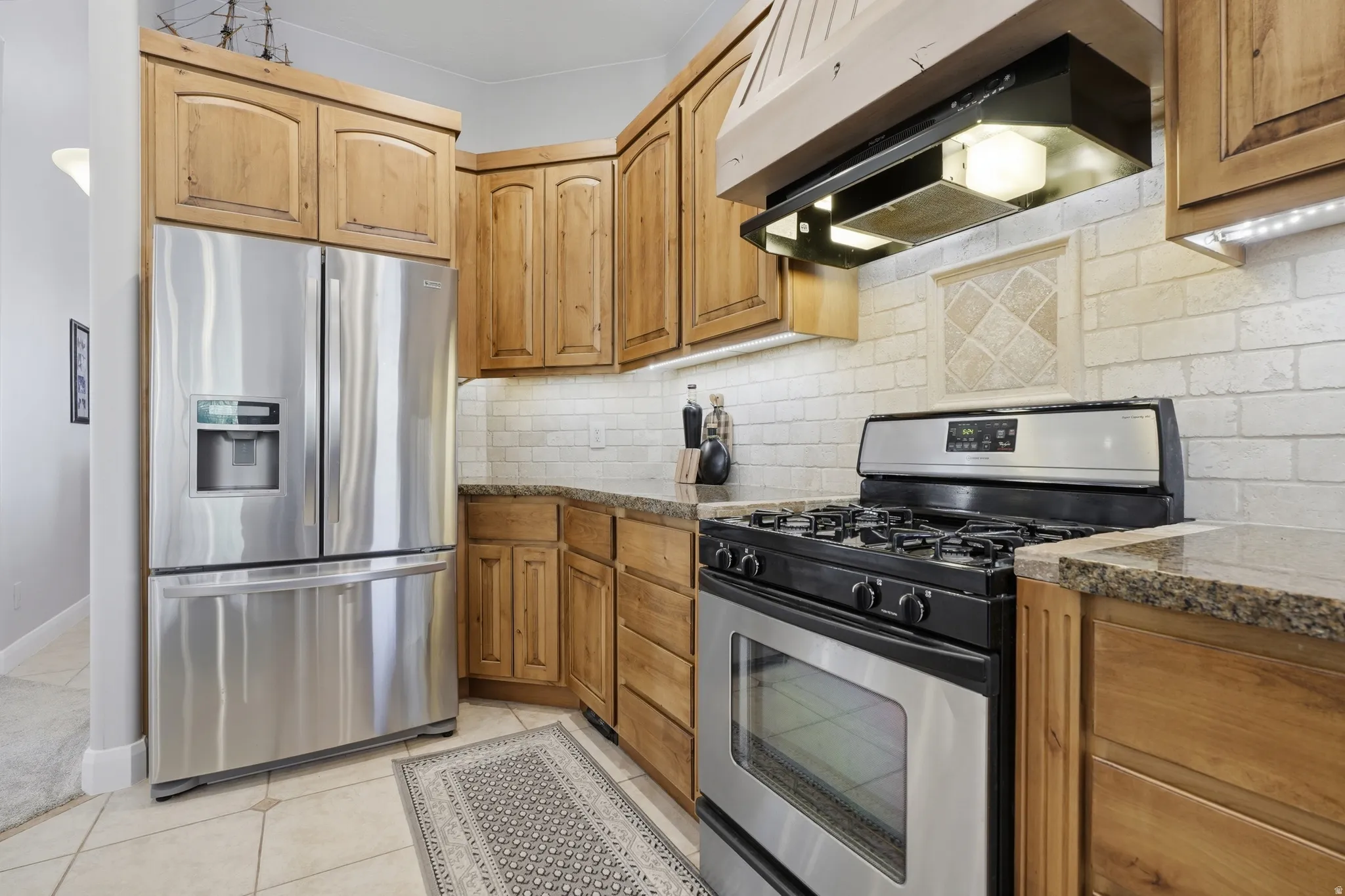 Kitchen featuring light-toned wood cabinetry, granite-finish countertops, and a subway tile backsplash