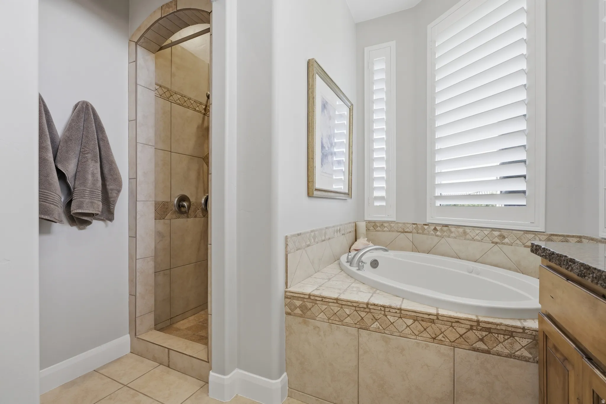Tiled walk-in shower with an arched entryway, featuring a built-in tub with surrounding tilework, and plantation shutters