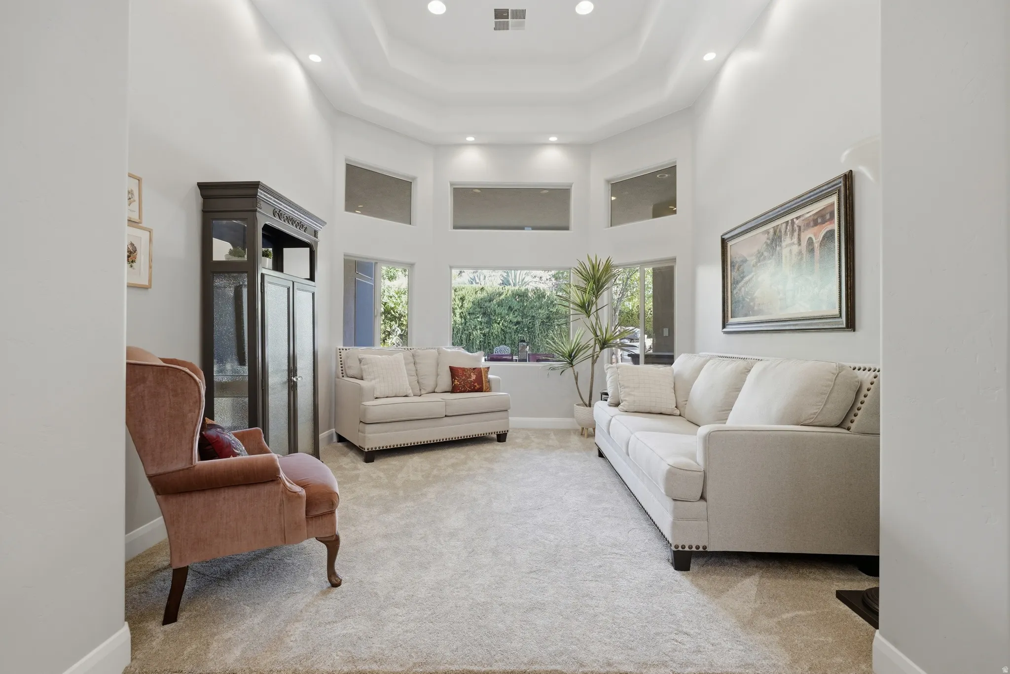 Spacious living area featuring a high tray ceiling with recessed lighting, large windows, and wall-to-wall carpeting