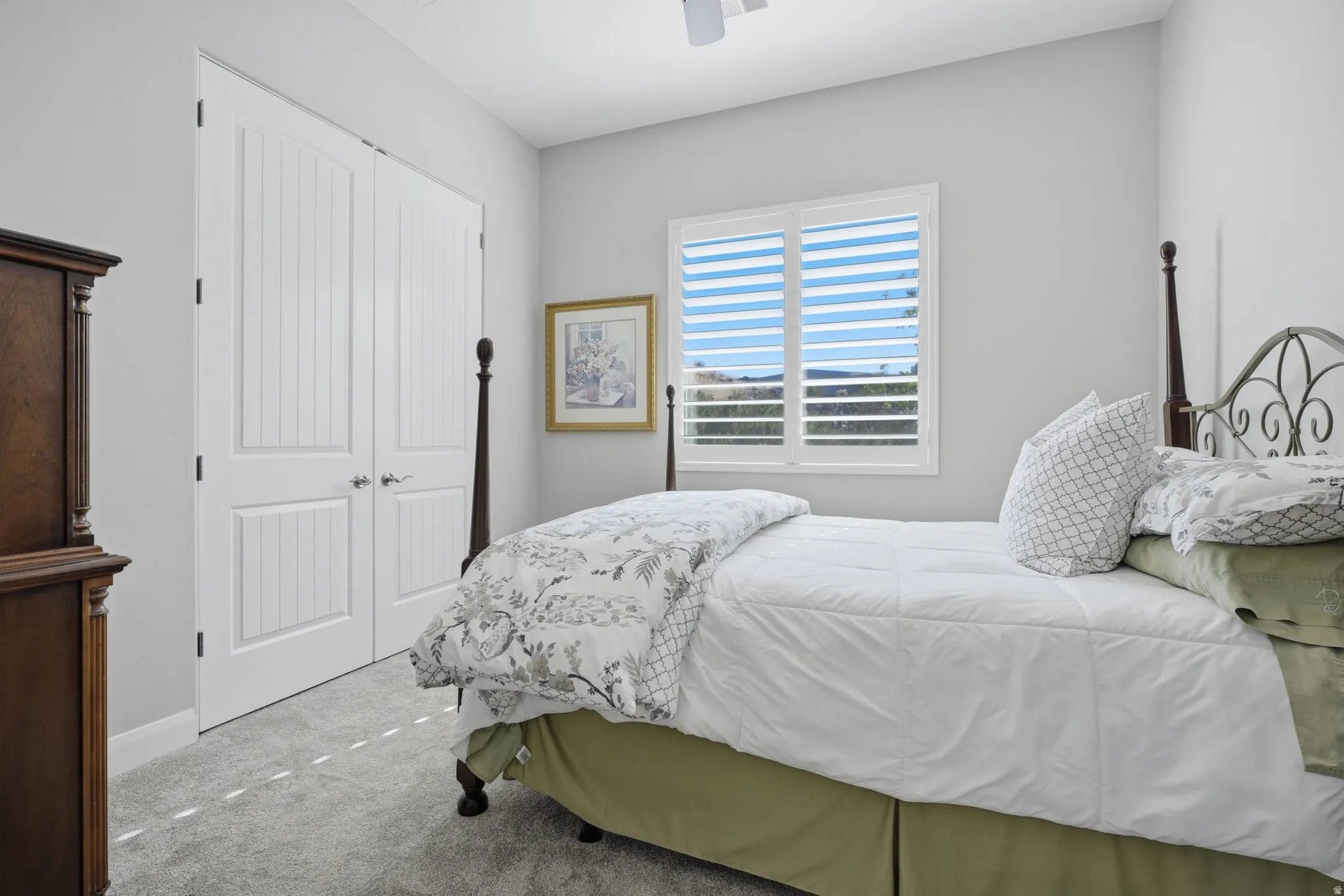 Bedroom featuring light gray walls, plush gray carpeting, a window with plantation shutters, and double bi-fold doors