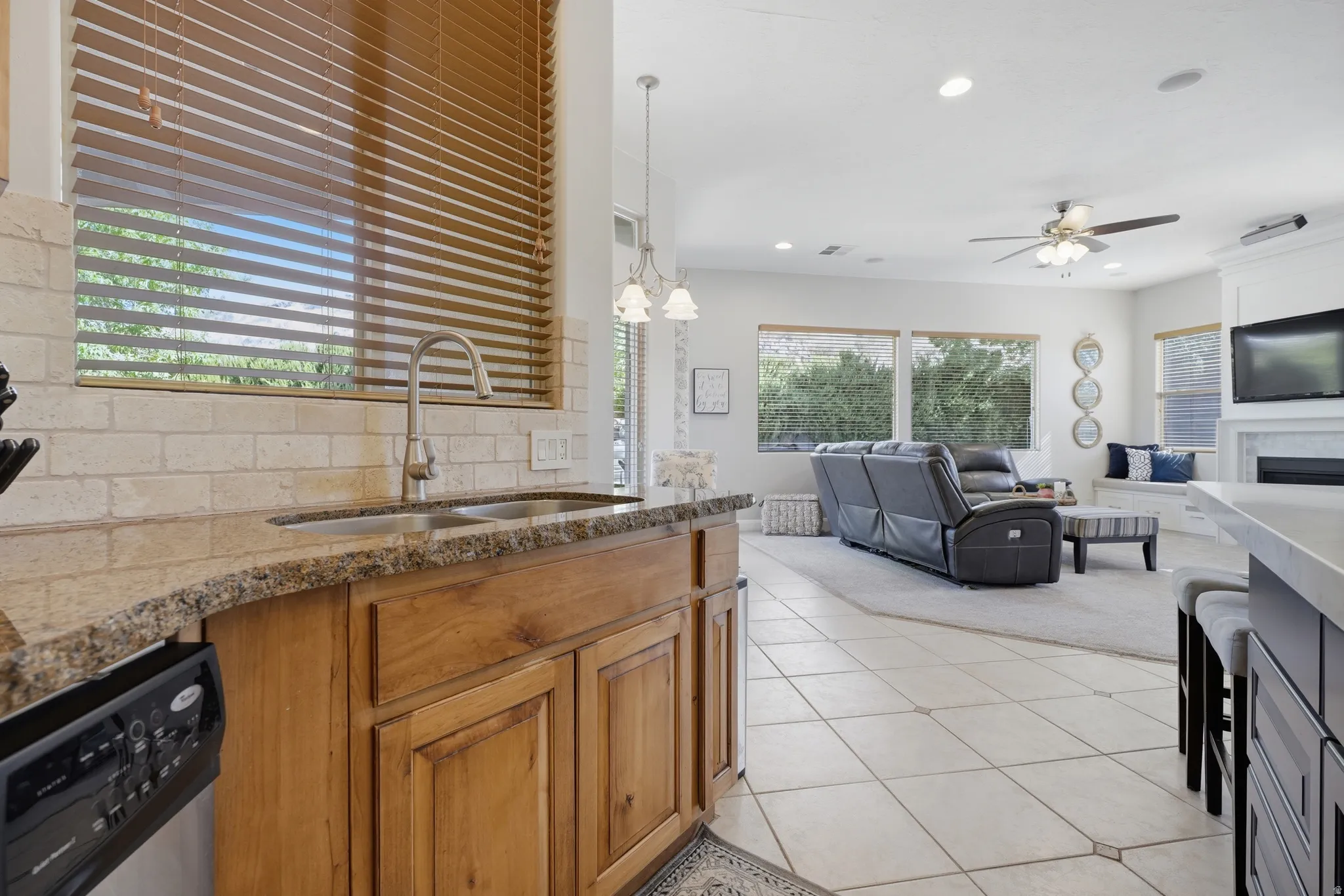 Kitchen area featuring a stainless steel double sink, granite countertops, stone-look tile backsplash, and wood cabinetry