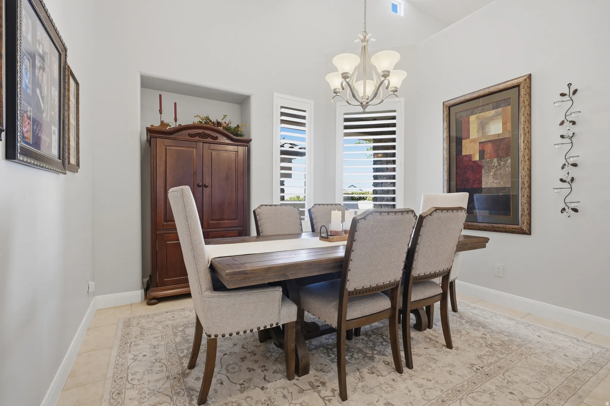 Spacious dining area featuring vaulted ceilings, plantation shutters, tile flooring, a built-in niche, and a multi-light chandelier