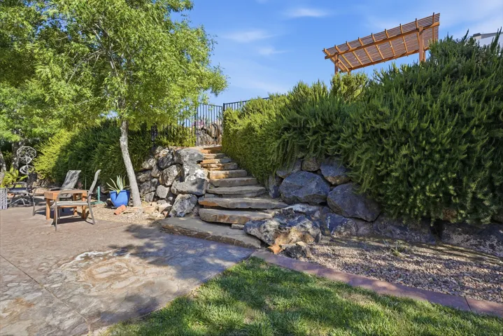 Stone retaining wall with natural stone steps leading to a raised area featuring a wood pergola