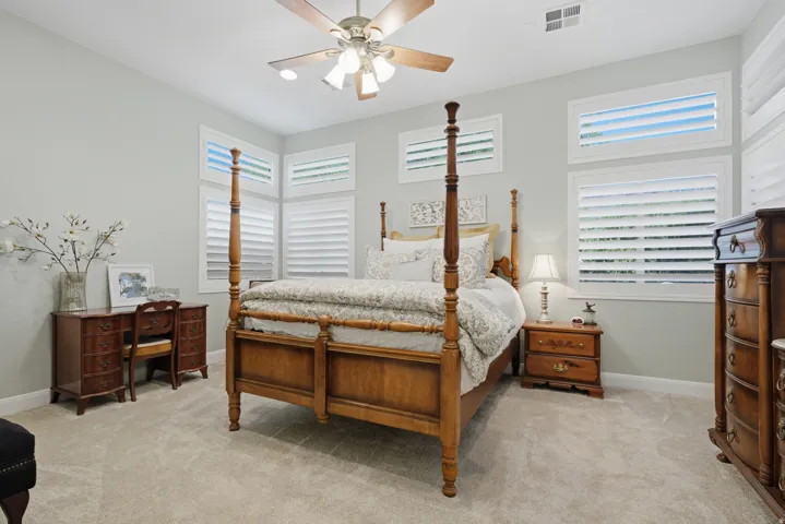 Carpeted room featuring multiple windows with louvered shutters, a ceiling fan with integrated lighting, and light-toned wall paint