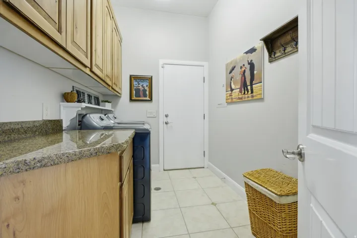 Functional laundry area featuring light wood cabinetry, stone-finish countertops, and tiled flooring