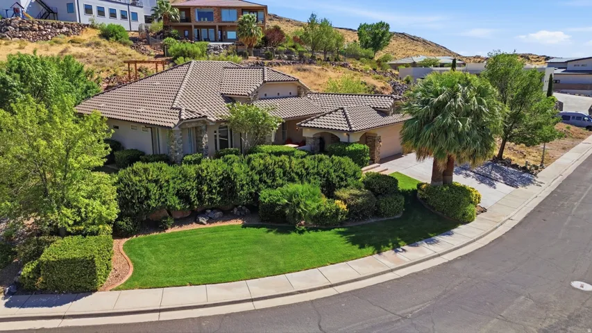 Custom home featuring a tile roof, stone facade accents, mature landscaping, a manicured lawn, and an integrated garage