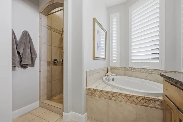 Tiled walk-in shower with an arched entryway, featuring a built-in tub with surrounding tilework, and plantation shutters