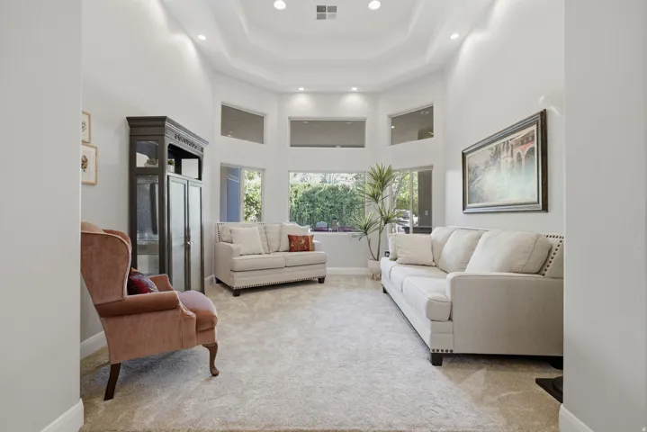 Spacious living area featuring a high tray ceiling with recessed lighting, large windows, and wall-to-wall carpeting
