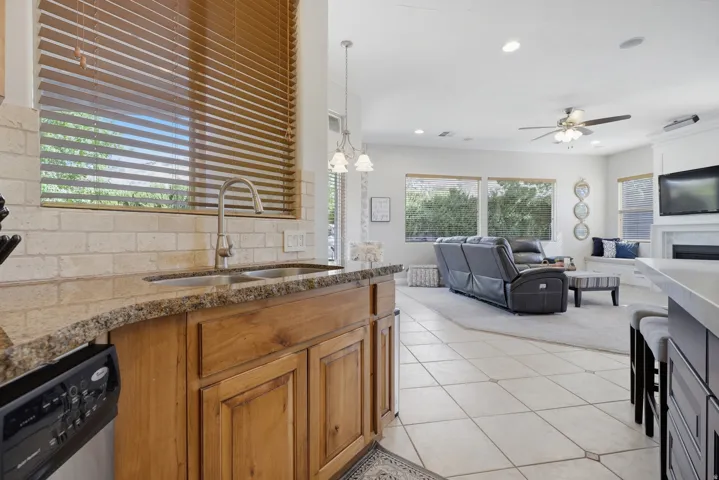 Kitchen area featuring a stainless steel double sink, granite countertops, stone-look tile backsplash, and wood cabinetry