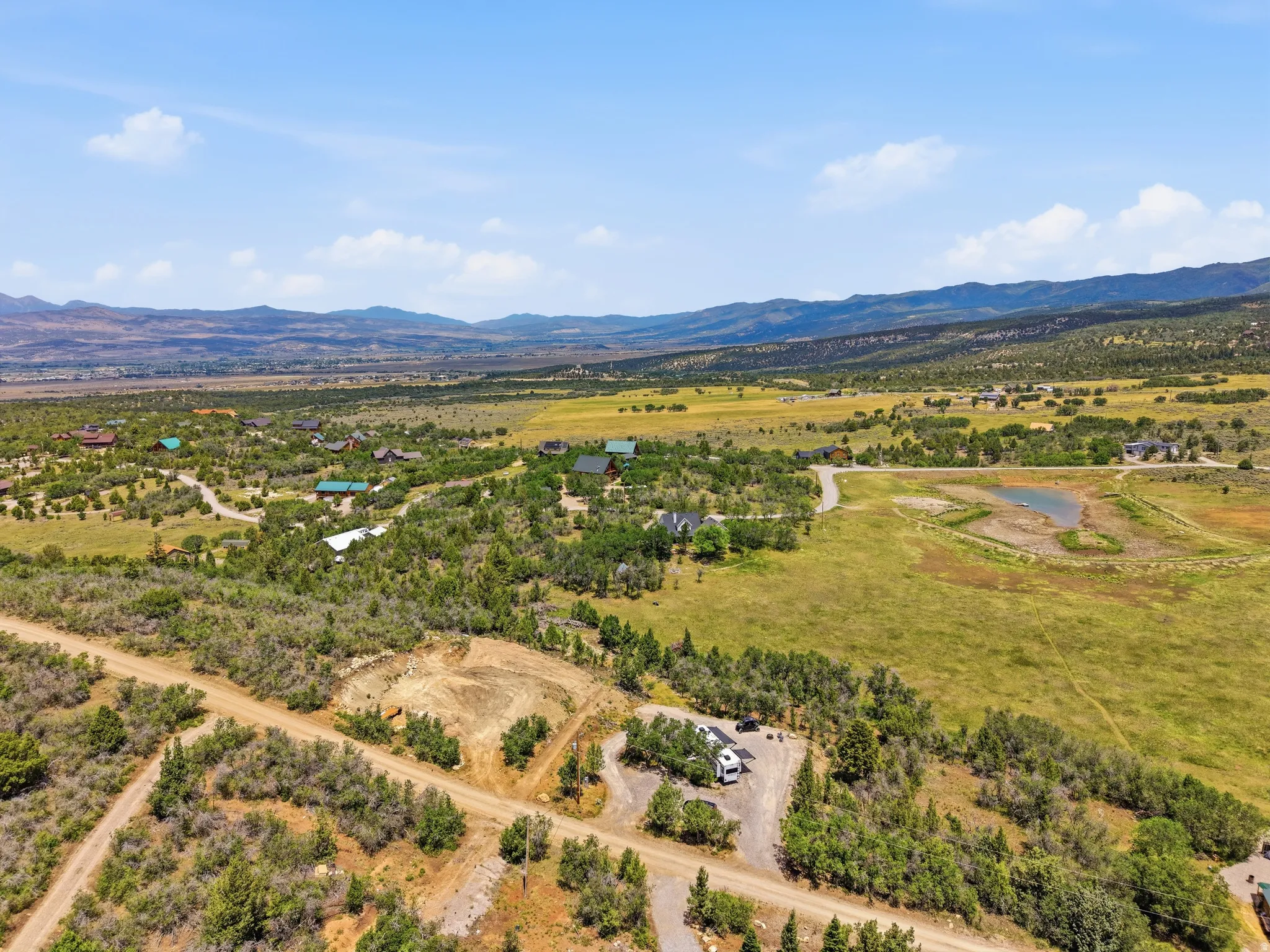 Expansive undeveloped land featuring natural foliage and a dirt road, offering a building site and distant mountain ranges