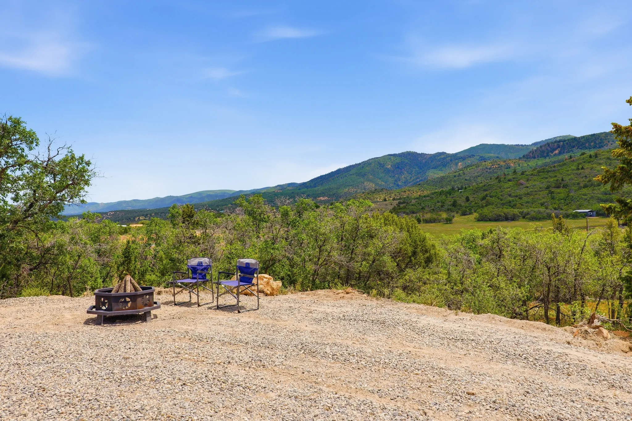 Gravel-surfaced outdoor area featuring a fire pit, surrounded by mature trees and natural mountain terrain