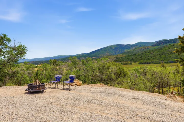 Gravel-surfaced outdoor area featuring a fire pit, surrounded by mature trees and natural mountain terrain