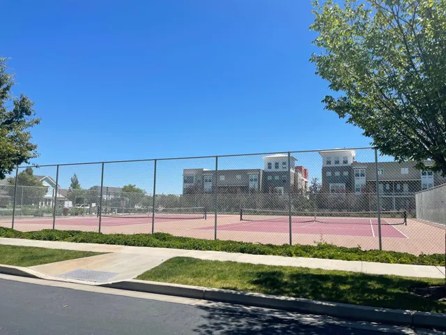 Community tennis courts featuring chain-link fencing, a hard court surface with painted lines, and a net system