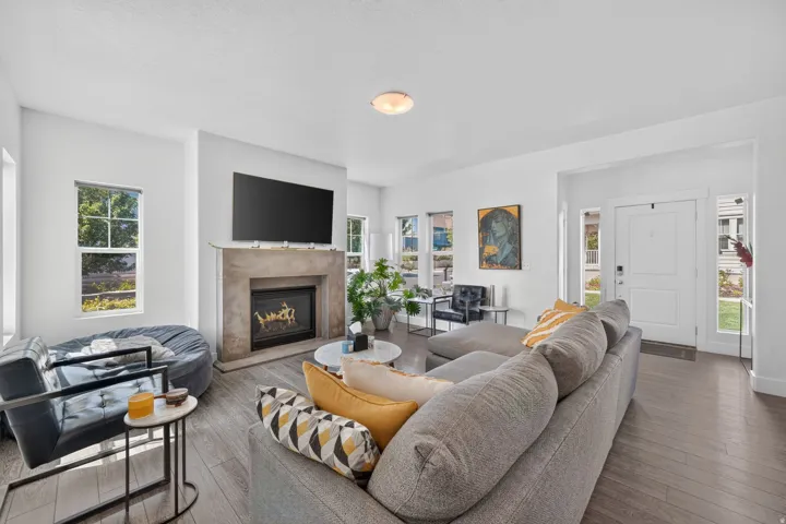 Spacious living area featuring light wood-finish flooring, a contemporary fireplace with a stone-finish surround, multiple windows, recessed lighting, and a white entry door with side-light windows