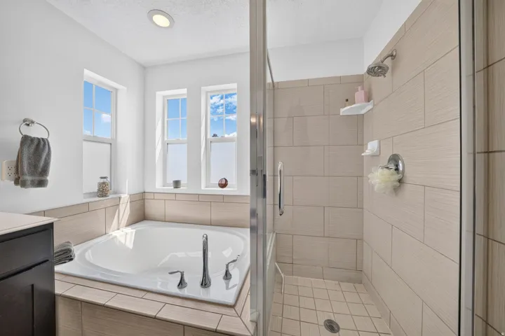 Modern bathroom featuring a built-in soaking tub with chrome fixtures, an adjacent walk-in shower with clear glass enclosure, and light-toned horizontal tile work