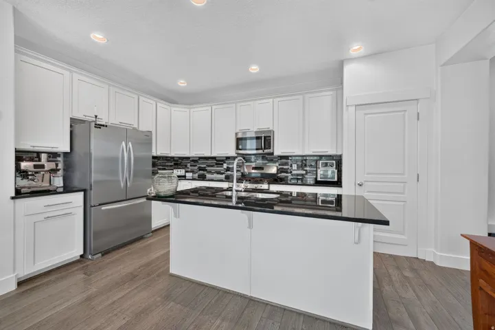 Kitchen featuring white cabinetry, dark countertops, a central island, stainless steel appliances, and wood-finish flooring