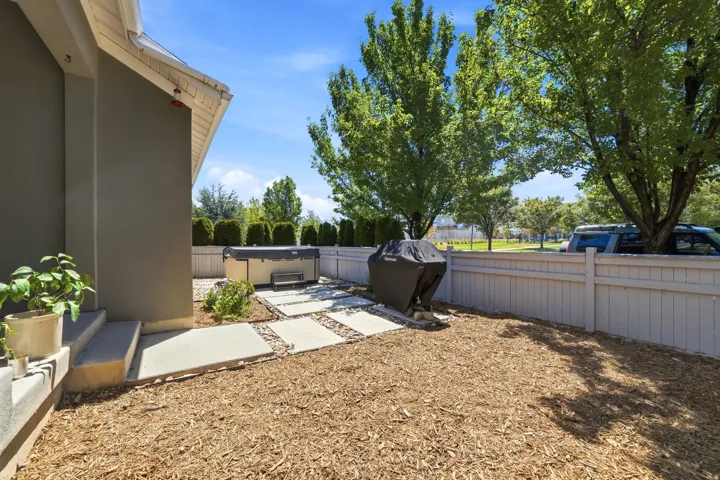 Private backyard featuring a hot tub, concrete paver path, wood chip ground cover, and a light-colored privacy fence
