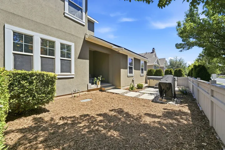 Private side yard featuring a stucco exterior, a covered patio, a white picket fence, and stepping stones