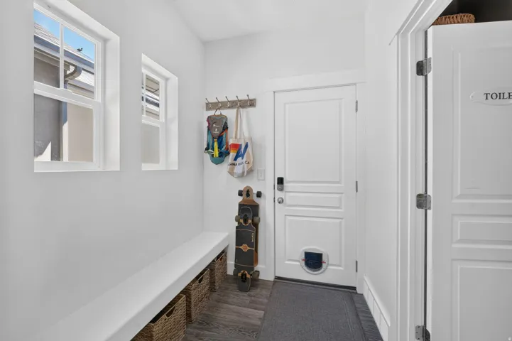 Entryway featuring two vertical windows, a built-in bench with storage space, a white paneled door with a pet door, and wood-finish flooring