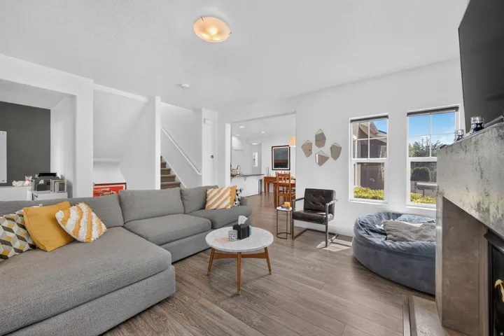 Spacious living area featuring wood-finish flooring, a fireplace with a stone surround, and multiple windows providing natural light