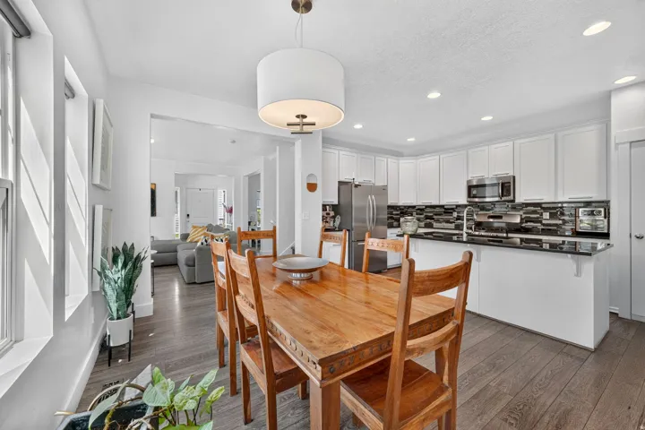 Open-concept living space featuring wood-finish flooring, a contemporary drum pendant light, white kitchen cabinetry, stainless steel appliances, and a tiled kitchen backsplash