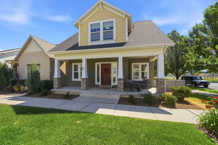Inviting two-story residence featuring a covered front porch with stone-clad columns, a red-paneled entry door, and a prominent dormer with shake siding