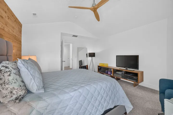 Vaulted ceiling bedroom featuring a modern ceiling fan, wood-panel accent wall, and neutral carpet flooring