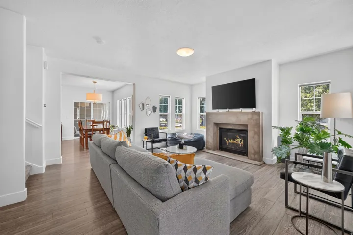 Living room featuring a fireplace with a stone surround, recessed lighting, wood-finish flooring, and multiple windows