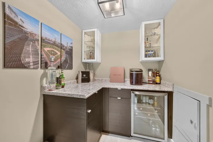 Corner wet bar featuring light granite countertops, dark wood-finish base cabinetry, and an integrated beverage refrigerator