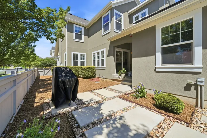 Exterior patio space featuring a concrete paver path, decorative river rock, and wood chip landscaping
