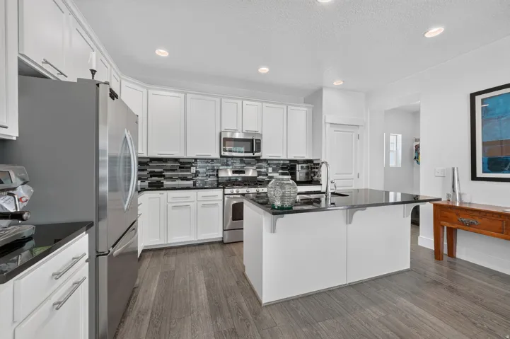 Kitchen featuring white cabinetry, stainless steel appliances, black countertops, a mosaic tile backsplash, and wood-finish flooring