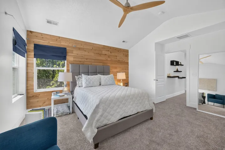 Bedroom featuring a wood-panel accent wall, vaulted ceiling, and a contemporary ceiling fan