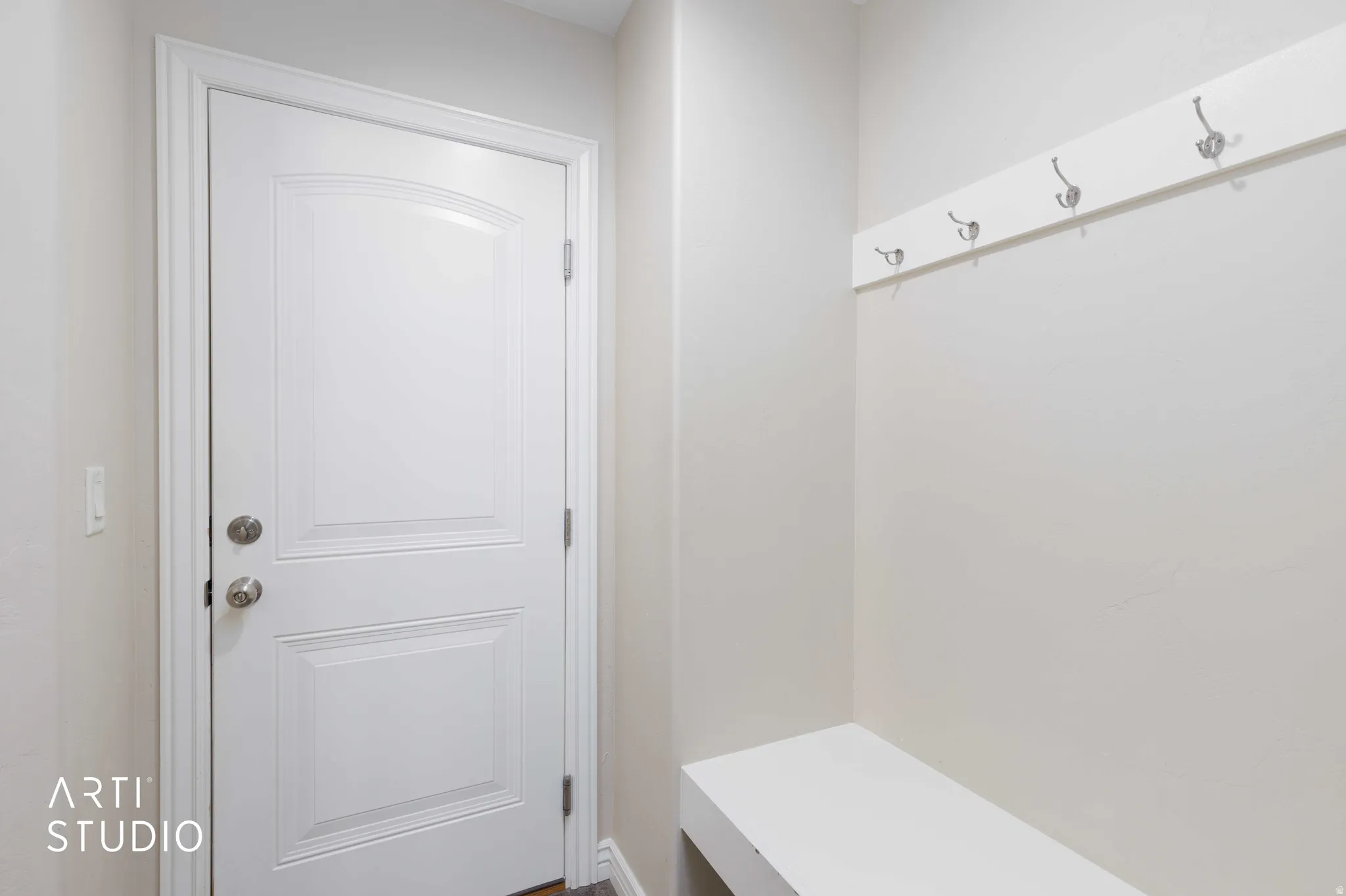 Entryway featuring a white paneled door with brushed nickel hardware, built-in white bench, and wall-mounted coat rack with chrome hooks