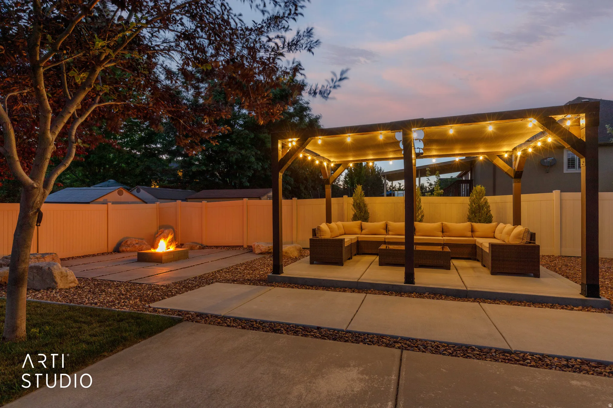 Outdoor living space featuring a dark wood pergola with string lighting, a concrete patio, a gravel hardscape, and a built-in fire pit