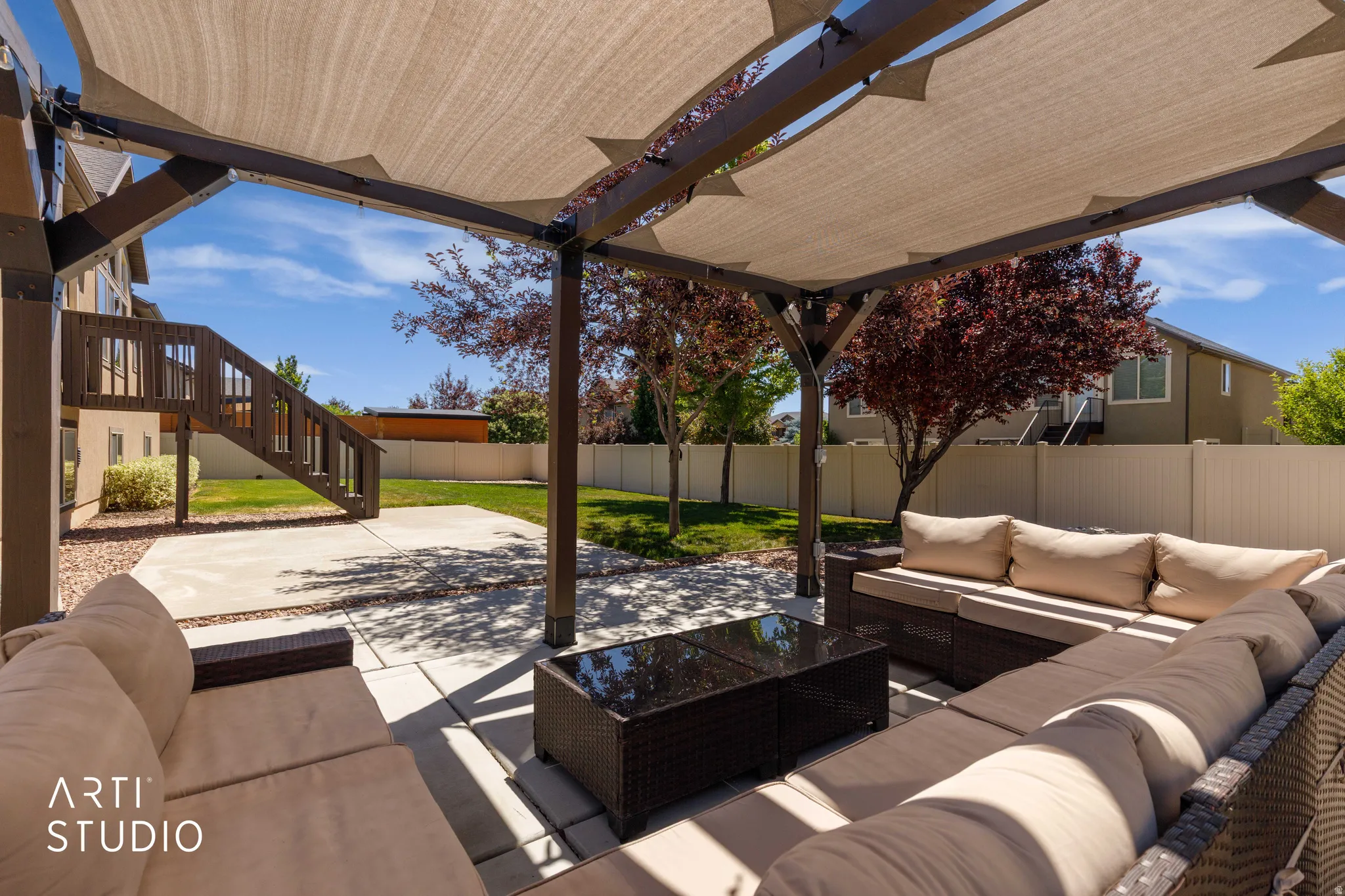 Covered patio area featuring a pergola with retractable shade, concrete patio flooring, and a fenced backyard with mature trees