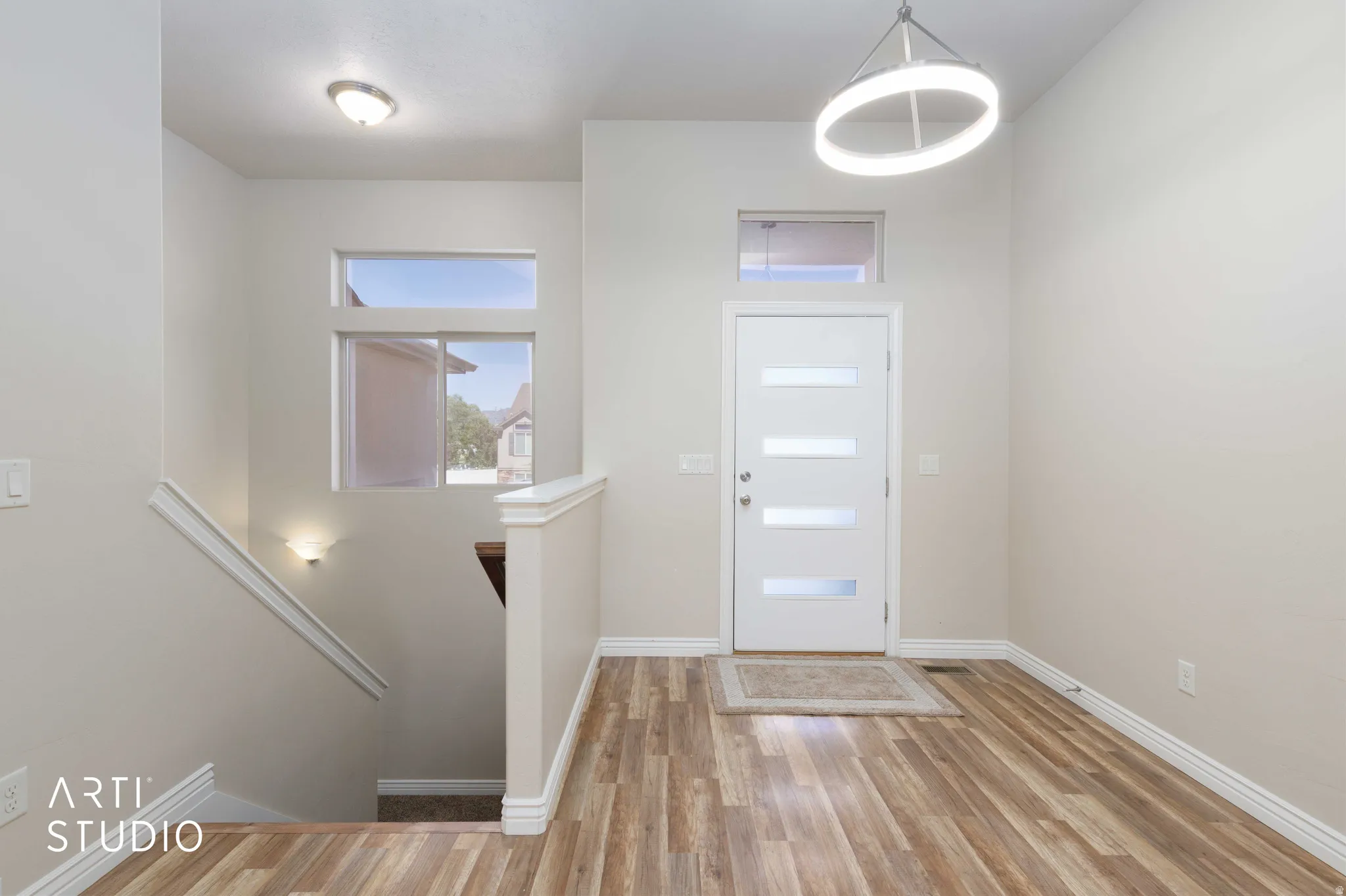 Entryway featuring wood-finish flooring, a contemporary white entry door with frosted glass panels, and a modern circular pendant light fixture
