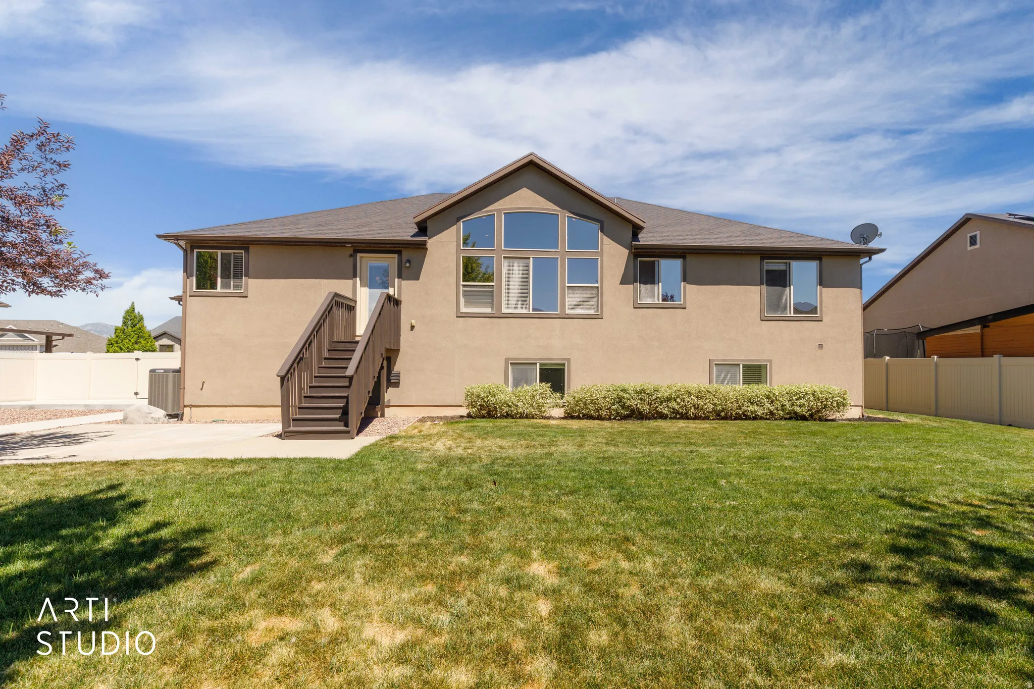 Rear exterior featuring a large grassy area, concrete patio, and exterior staircase with dark wood-finish railings