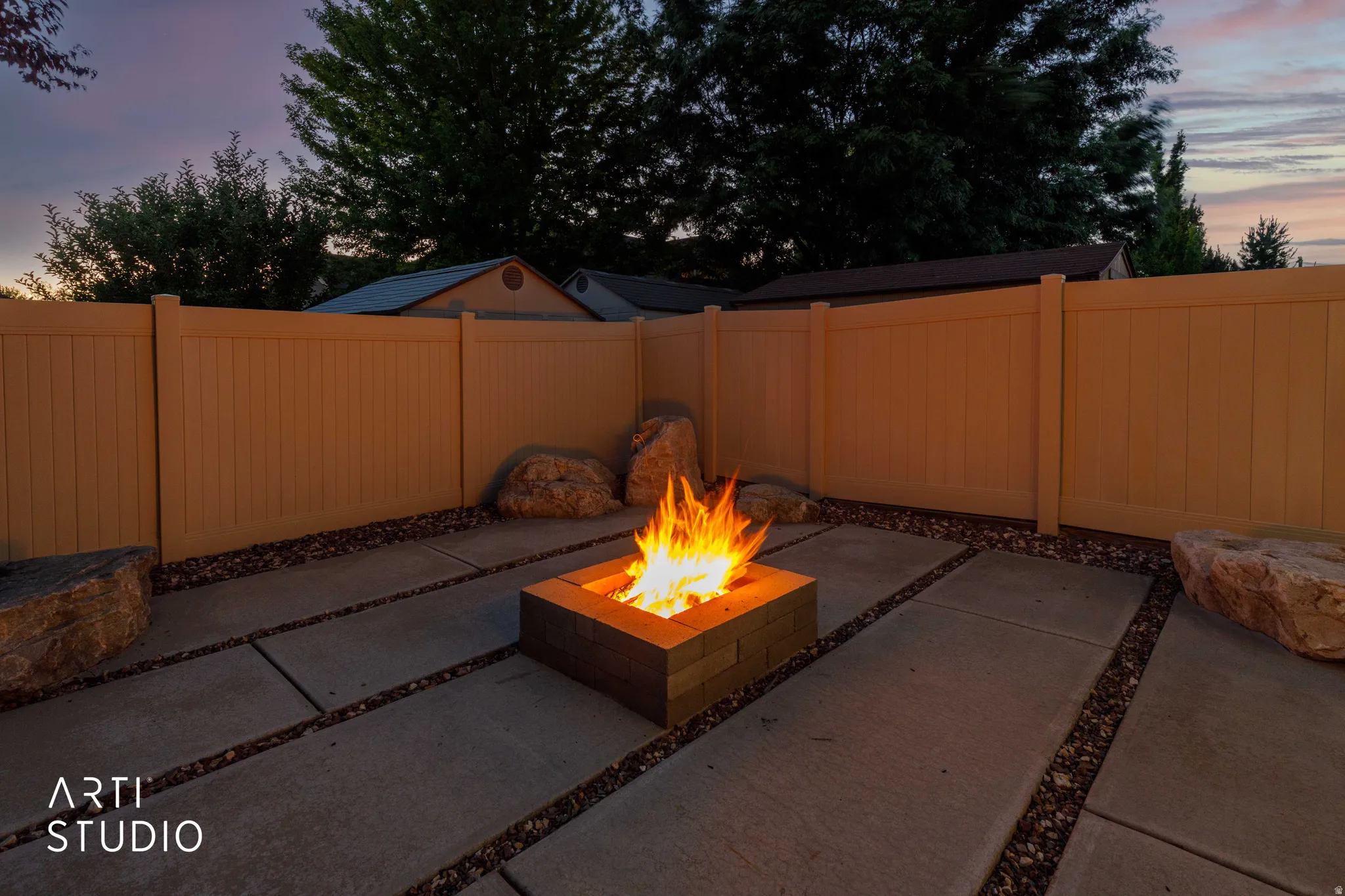 Outdoor patio featuring a built-in fire pit, concrete paver sections, and dark aggregate ground cover