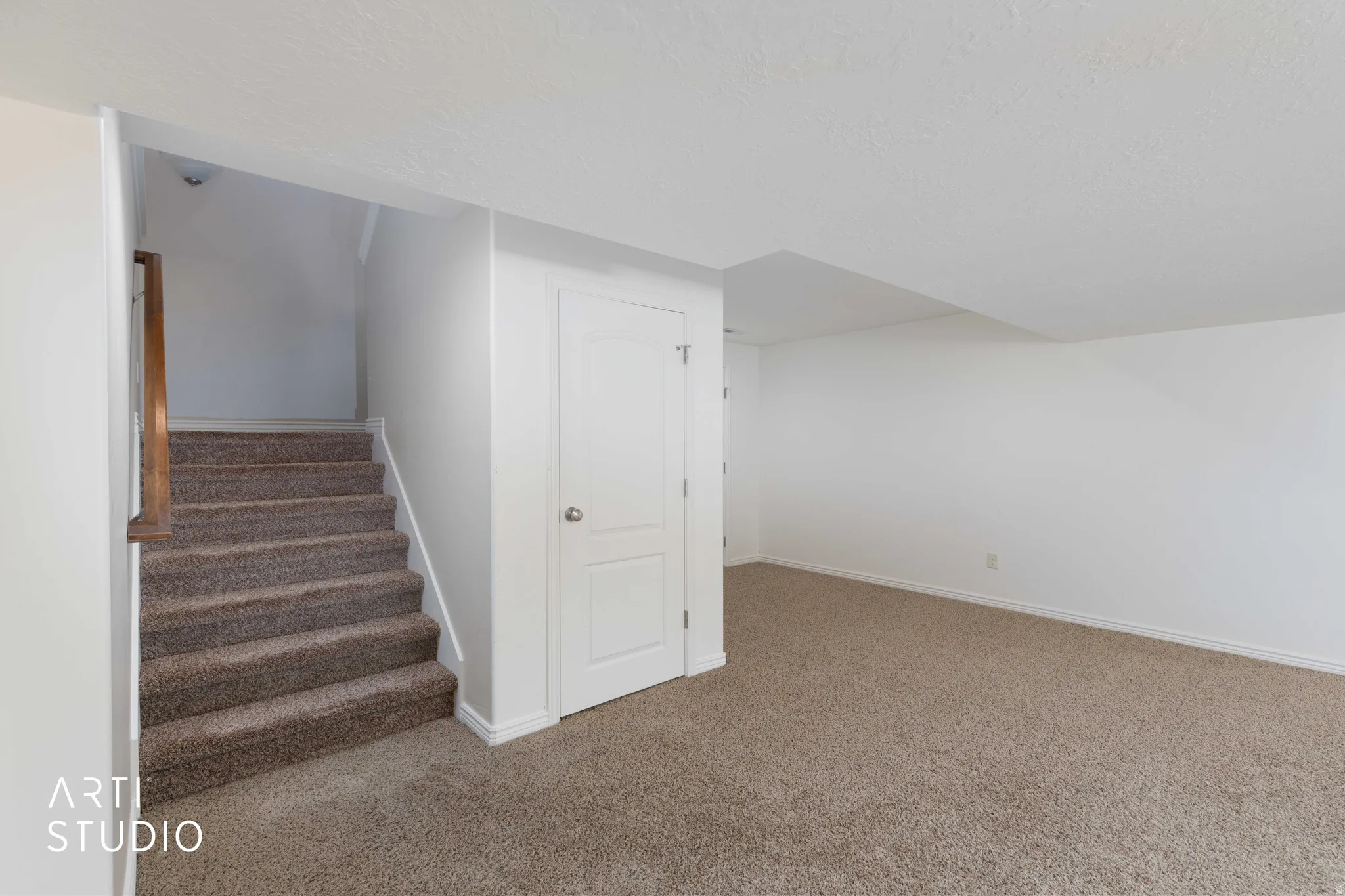 Carpeted staircase with wood handrail, white walls, and neutral carpet flooring