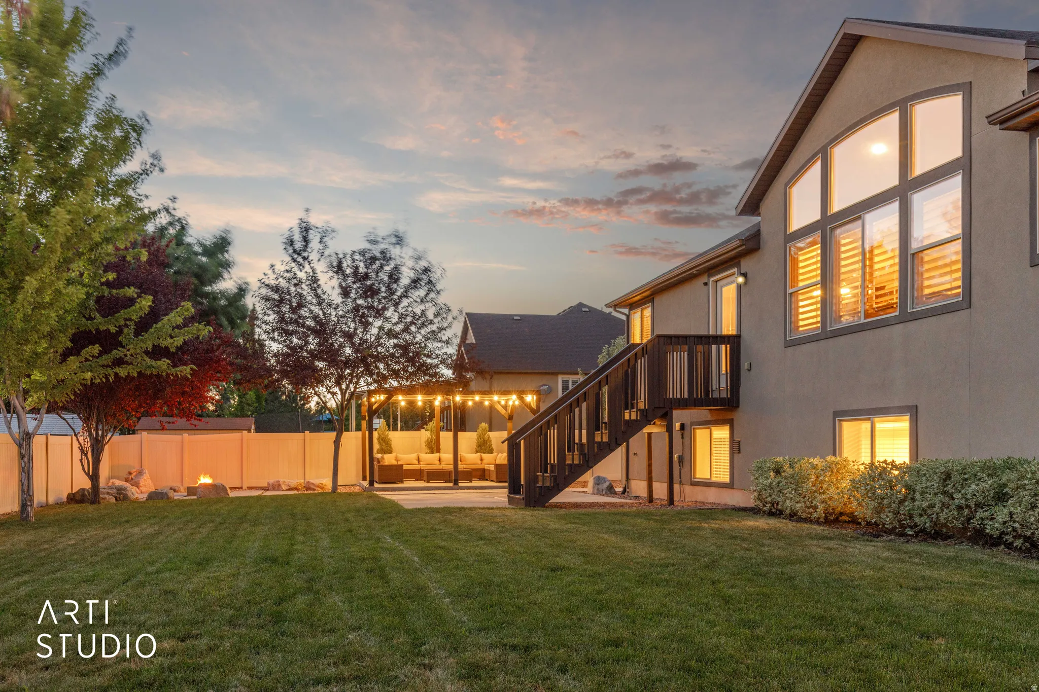 Expansive backyard featuring a large green lawn, a dedicated fire pit area, and mature perimeter trees