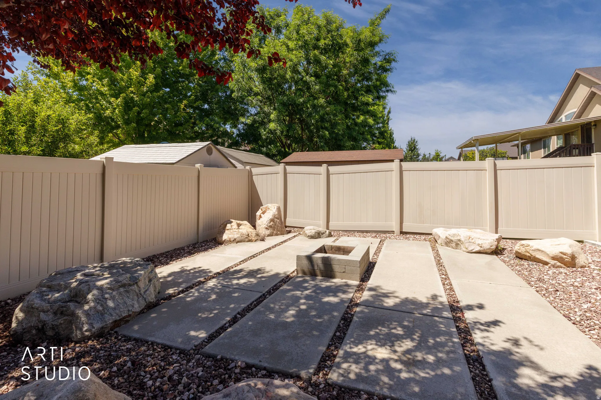 Outdoor living area featuring a built-in fire pit, stone elements, expansive concrete paver pathways, and a gravel ground cover