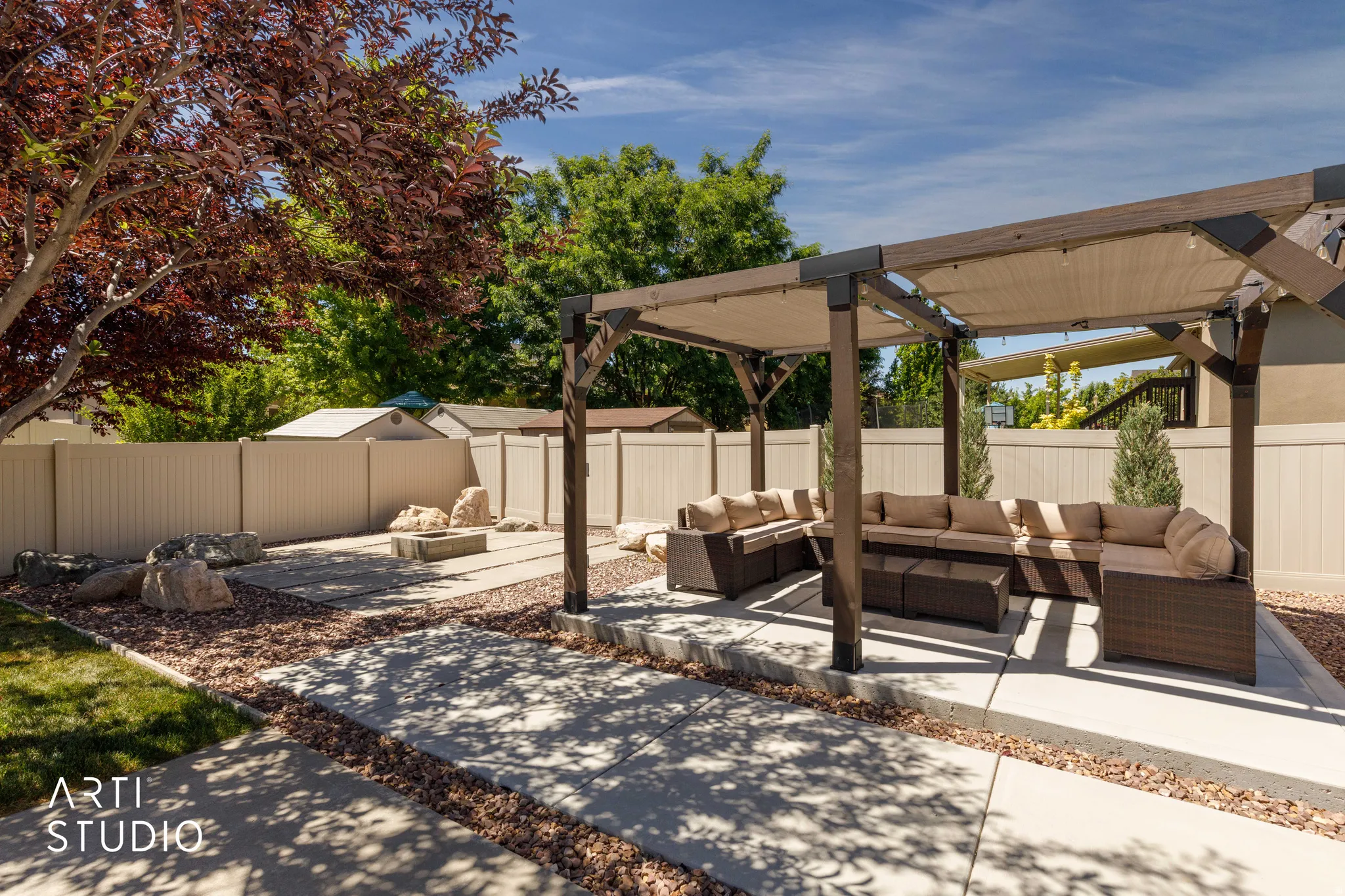 Outdoor pergola with retractable fabric shades, concrete patio, a gravel border, and a concrete fire pit area with stone accents